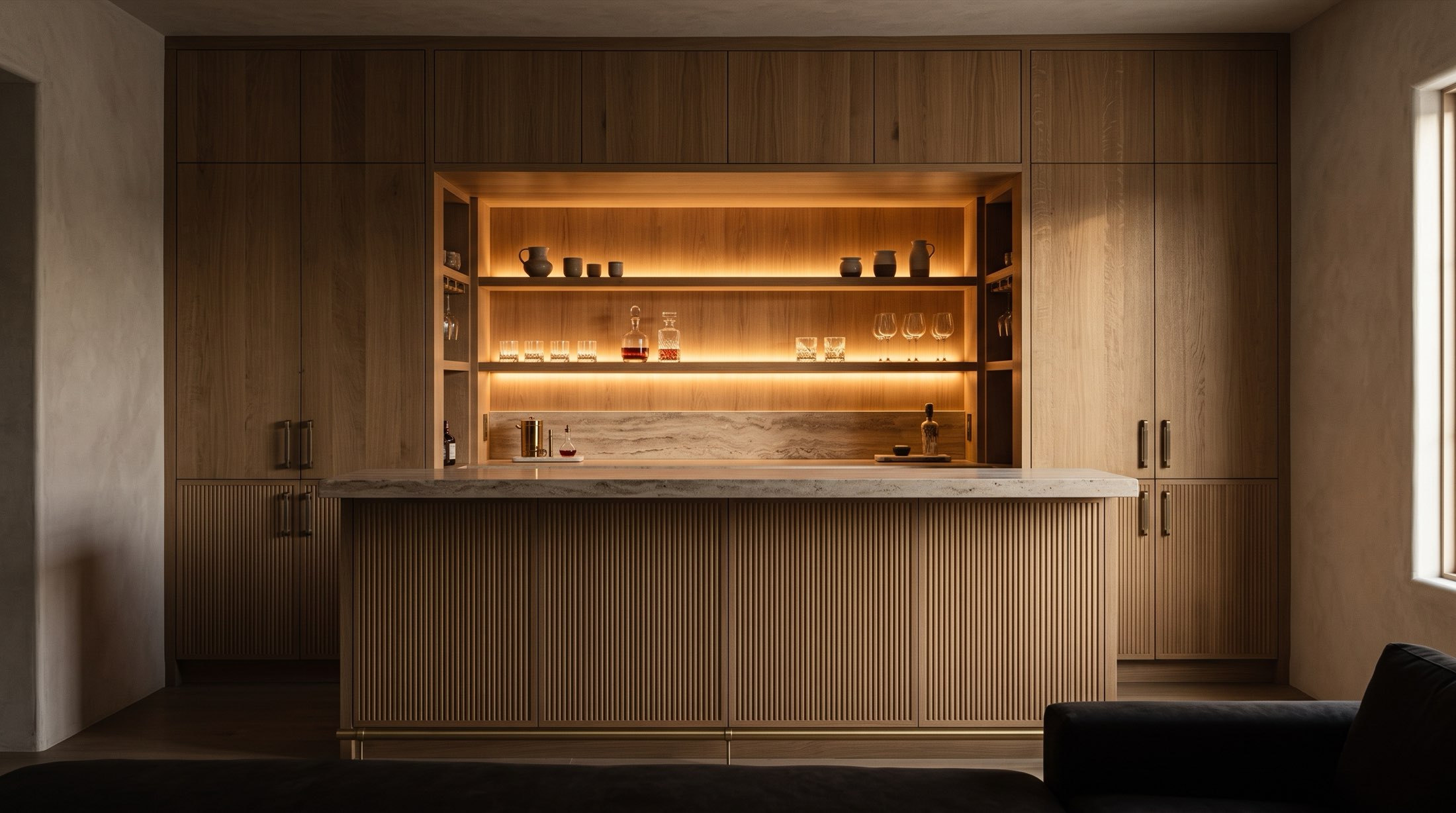 Full-wall white oak home bar with fluted doors, lit shelves and a travertine counter